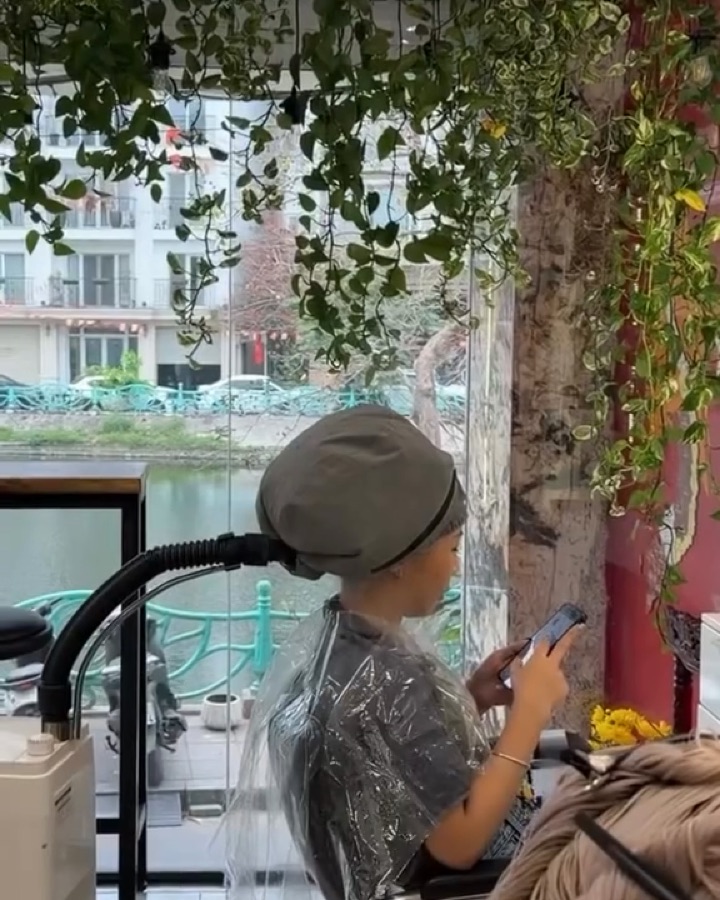 Khách ngồi ủ tóc cạnh ô kính nhìn ra hồ, xung quanh là cây leo